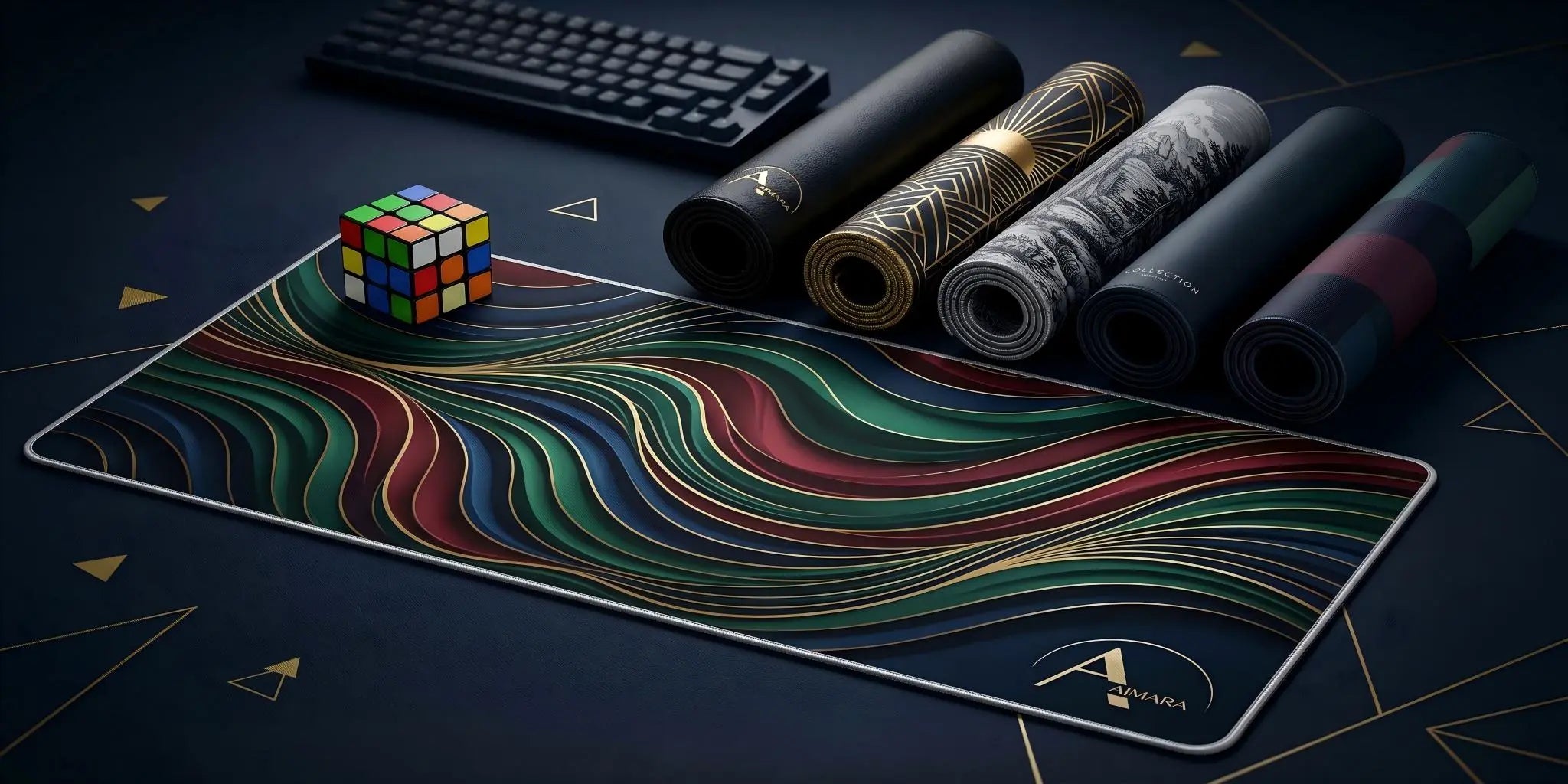 AIMARA premium extended desk mat with jewel-tone 3D wavy pattern, next to a colourful Rubik's cube, a mechanical keyboard, and other rolled mats on a dark navy surface with gold geometric accents.